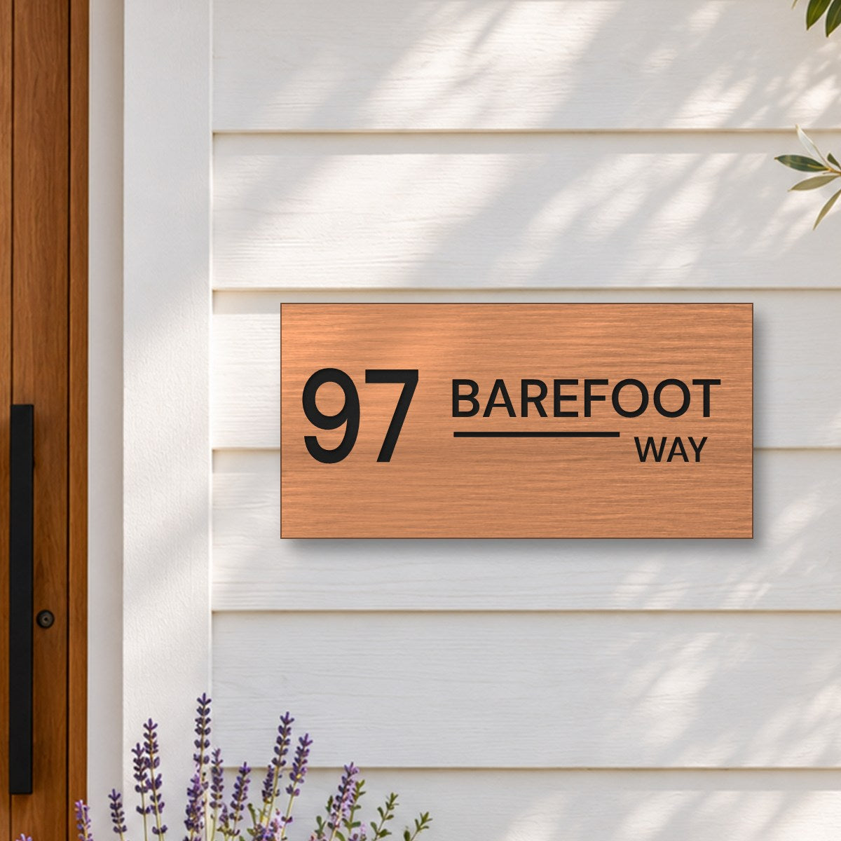 Brushed copper house number and street name sign with a brushed metal look, The Alexandra, reading 97 Barefoot Way in black lettering, on white weatherboards beside a timber front door, with lavender and an olive tree.