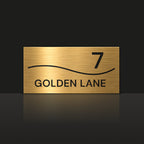 Brushed gold house number and street name sign with a brushed metal look, The Bokarina, reading 7 Golden Lane in black lettering, with a wave line.