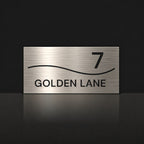 Brushed silver house number and street name sign with a brushed metal look, The Bokarina, reading 7 Golden Lane in black lettering, with a wave line.