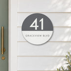 Matte round house number and street name sign reading 41 Graceview Blvd, with a matte charcoal top half and a white number, over a white bottom half and a charcoal street name, The Buddina style, on white weatherboards beside a sage green front door.