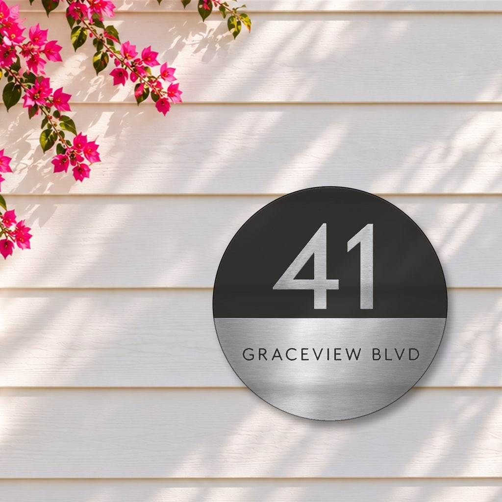 Silver round house number and street name sign reading 41 Graceview Blvd, with a black top half and a silver number, over a brushed silver bottom half and a black street name, The Buddina style, on white weatherboards under a pink bougainvillea.