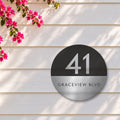 Silver round house number and street name sign reading 41 Graceview Blvd, with a black top half and a silver number, over a brushed silver bottom half and a black street name, The Buddina style, on white weatherboards under a pink bougainvillea.