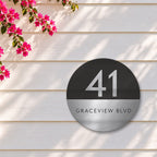 Silver round house number and street name sign reading 41 Graceview Blvd, with a black top half and a silver number, over a brushed silver bottom half and a black street name, The Buddina style, on white weatherboards under a pink bougainvillea.