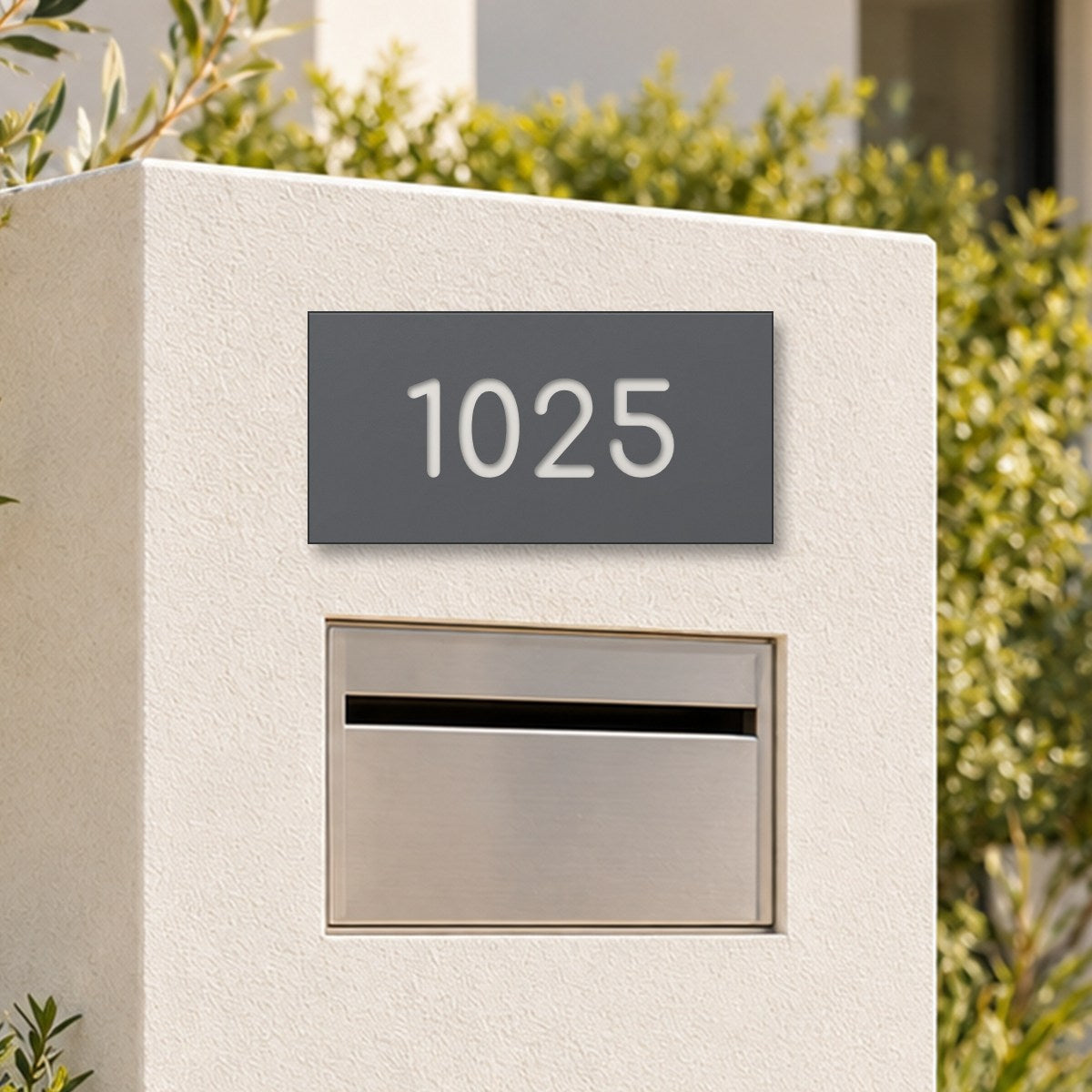 Matte charcoal house number sign, The Kawana, with the number 1025 in white lettering, on a white rendered pillar above a letterbox.