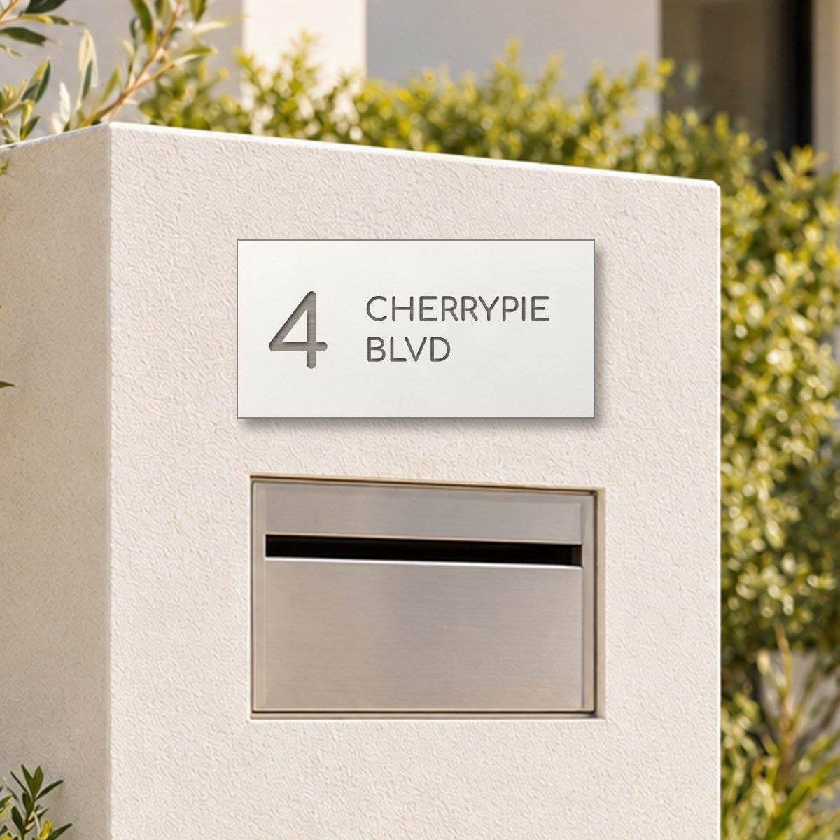 Brushed silver house number and street name sign with a brushed metal look, The Maleny, white face reading 4 Cherrypie Blvd in silver lettering, on a white rendered pillar above a letterbox.