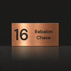 Brushed copper house number and street name sign with a brushed metal look, The Marcoola, reading 16 Babalon Chase in black lettering.