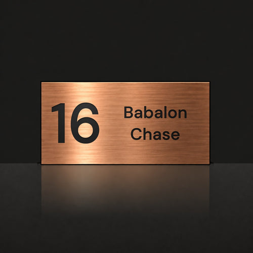 Brushed copper house number and street name sign with a brushed metal look, The Marcoola, reading 16 Babalon Chase in black lettering.