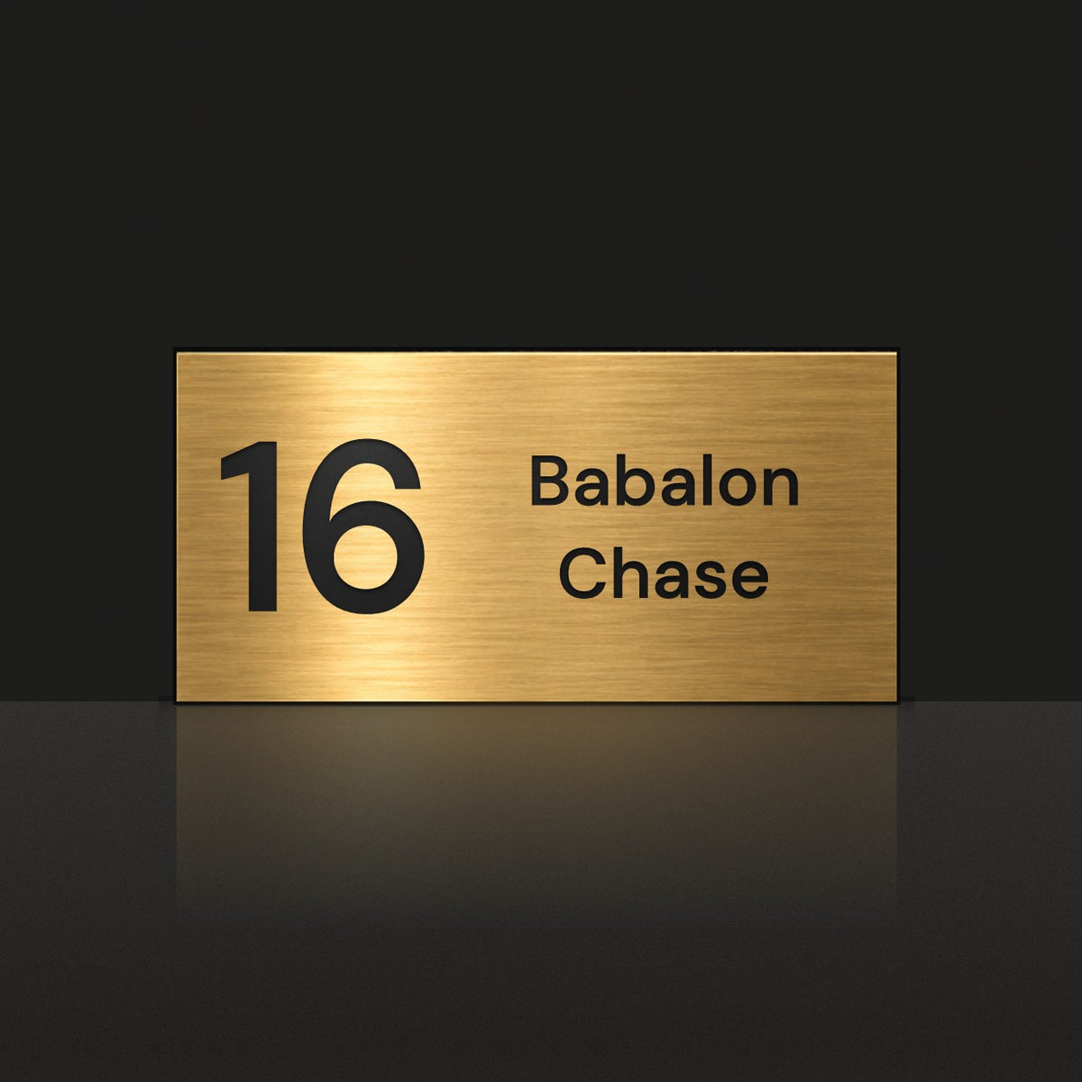 Brushed gold house number and street name sign with a brushed metal look, The Marcoola, reading 16 Babalon Chase in black lettering.