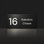 Matte black house number and street name sign, The Marcoola, reading 16 Babalon Chase in white lettering.