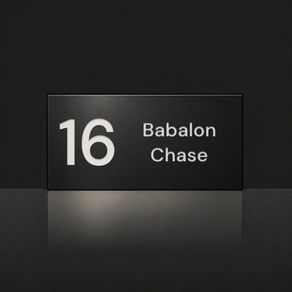 Matte black house number and street name sign, The Marcoola, reading 16 Babalon Chase in white lettering.