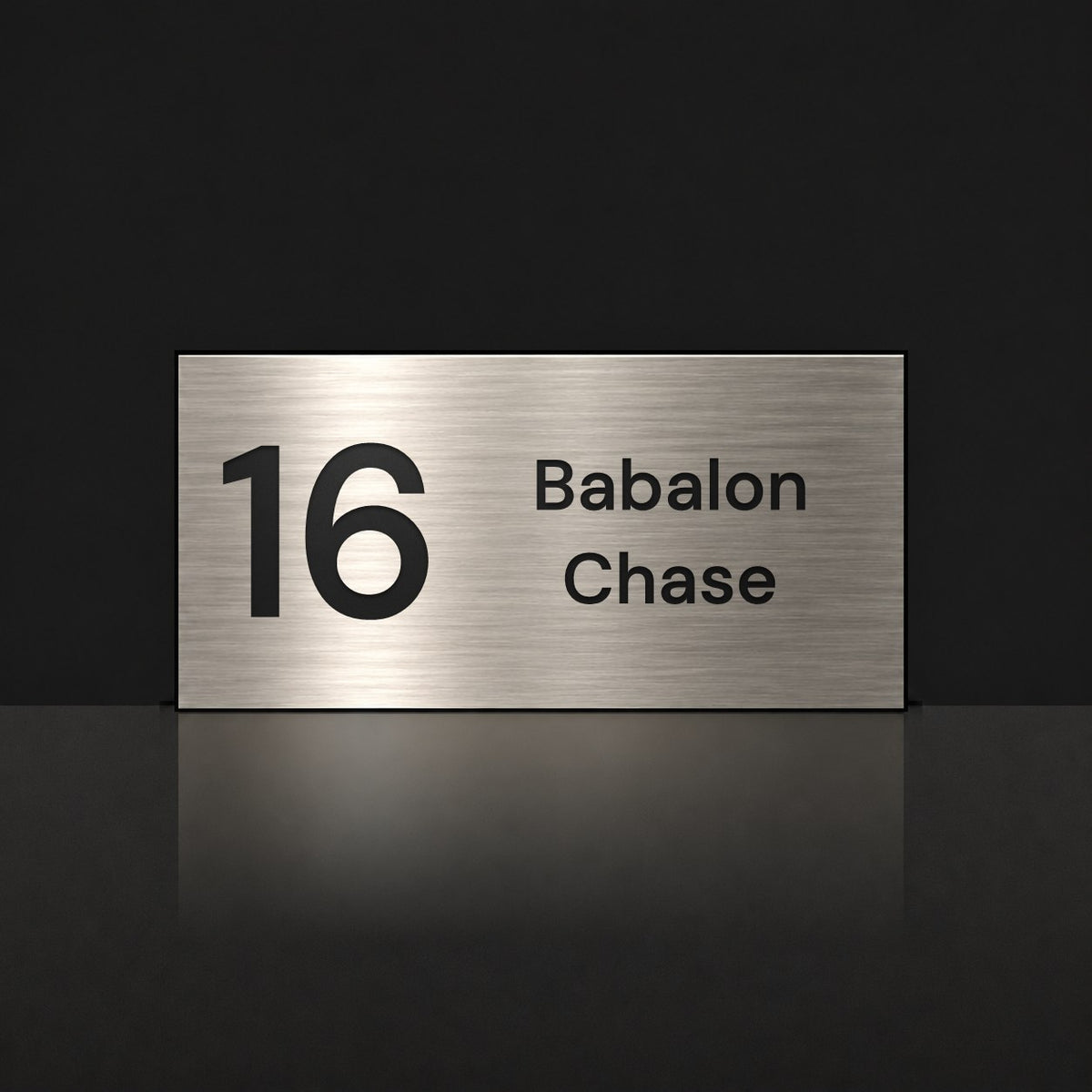 Brushed silver house number and street name sign with a brushed metal look, The Marcoola, reading 16 Babalon Chase in black lettering.