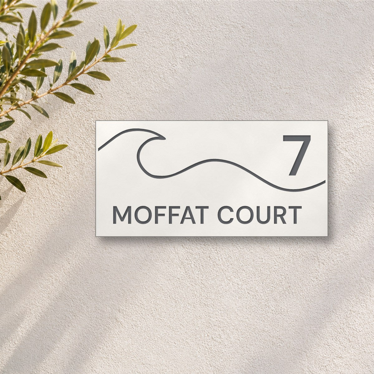Matte white house number and street name sign, The Moffat, reading 7 Moffat Court in charcoal lettering, with a wave, on a white rendered wall with olive branches.