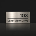 Brushed silver house number and street name sign with a brushed metal look, The Noosa, reading 103 Lake View Drive in black lettering.