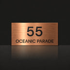 Brushed copper house number and street name sign with a brushed metal look, The Peregian, reading 55 Oceanic Parade in black lettering.