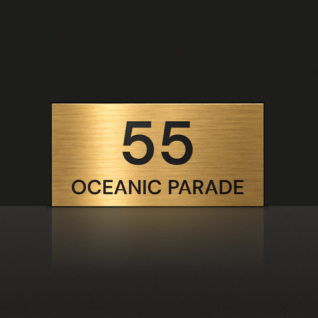 Brushed gold house number and street name sign with a brushed metal look, The Peregian, reading 55 Oceanic Parade in black lettering.