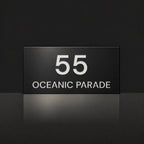 Matte black house number and street name sign, The Peregian, reading 55 Oceanic Parade in white lettering.