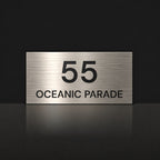 Brushed silver house number and street name sign with a brushed metal look, The Peregian, reading 55 Oceanic Parade in black lettering.