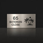 Brushed silver house number and street name sign with a brushed metal look, The Yaroomba, reading 65 Bateman Close in black lettering, with palm trees and a sun.