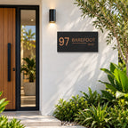 Brushed copper house number and street name sign with a brushed metal look, The Alexandra, black face reading 97 Barefoot Way in copper lettering, mounted on a white rendered wall beside a timber front door.