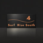 Brushed copper house number and street name sign with a brushed metal look, The Bokarina, black face reading 4 Surf Rise South in copper lettering, with a wave line.