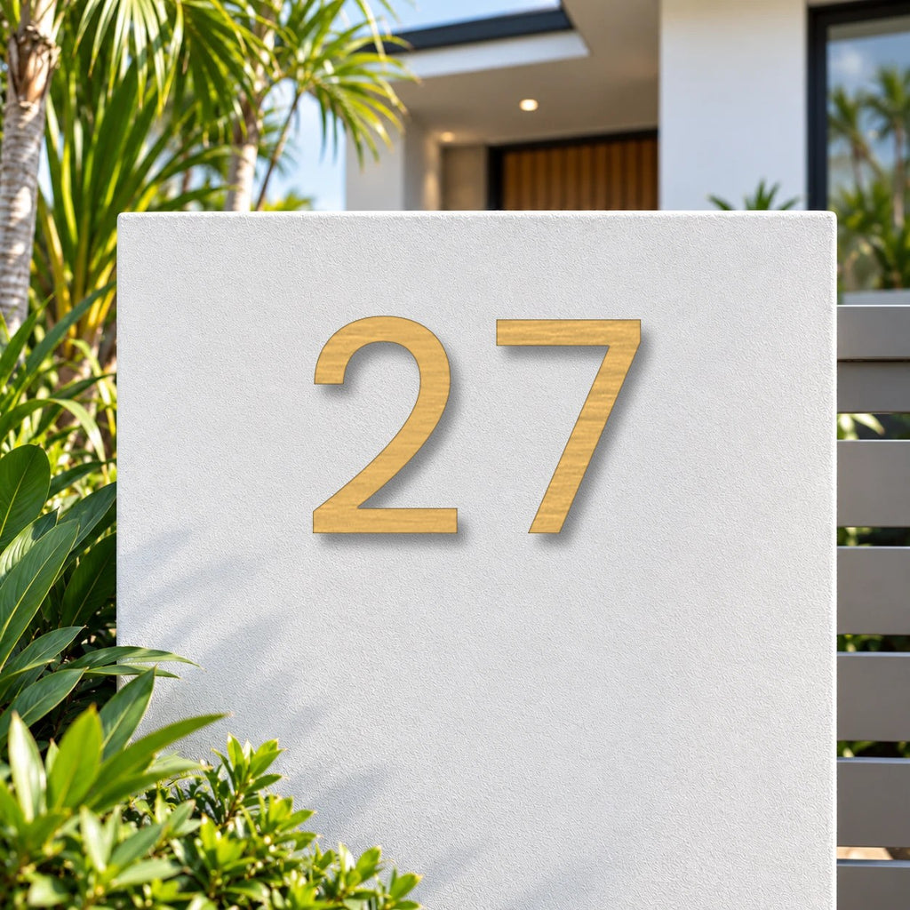 Brushed gold floating acrylic house number 27 in the modern font on invisible standoffs, on a white rendered front pillar.