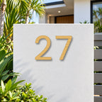 Brushed gold floating acrylic house number 27 in the modern font on invisible standoffs, on a white rendered front pillar.