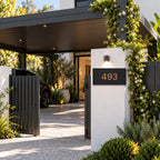 Brushed copper house number sign with a brushed metal look, The Kawana, black face with the number 493 in copper lettering, mounted on a white rendered pillar beside a black carport gate.