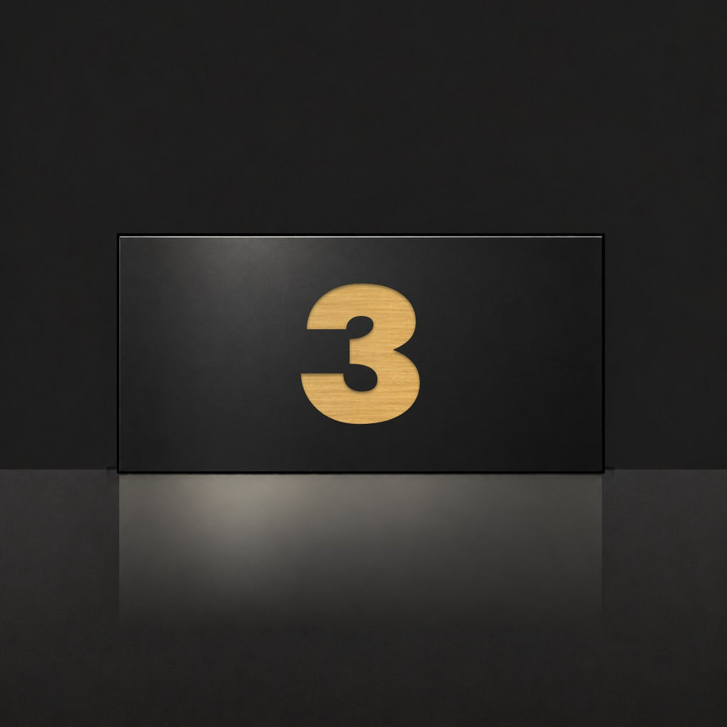 Brushed gold house number sign with a brushed metal look, The Kawana, black face with the number 3 in gold lettering.