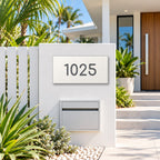 Matte white house number sign, The Kawana, with the number 1025 in charcoal lettering, mounted on a white rendered fence above a white letterbox.