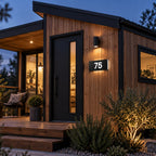 Matte black illuminated house number sign, The Kawana, mounted on timber cladding beside a black front door at dusk, the number 75 lit from behind.