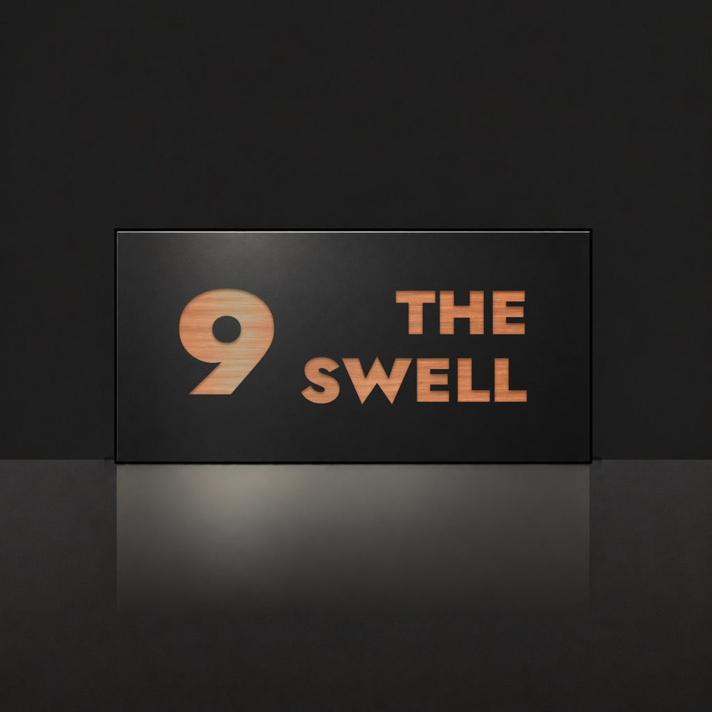 Brushed copper house number and street name sign with a brushed metal look, The Marcoola, black face reading 9 The Swell in copper lettering.