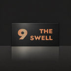 Brushed copper house number and street name sign with a brushed metal look, The Marcoola, black face reading 9 The Swell in copper lettering.