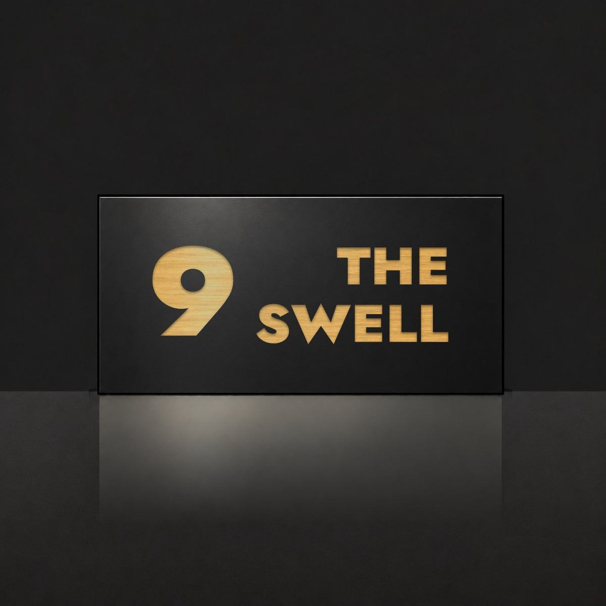 Brushed gold house number and street name sign with a brushed metal look, The Marcoola, black face reading 9 The Swell in gold lettering.
