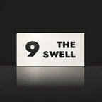 Matte white house number and street name sign, The Marcoola, reading 9 The Swell in black lettering.