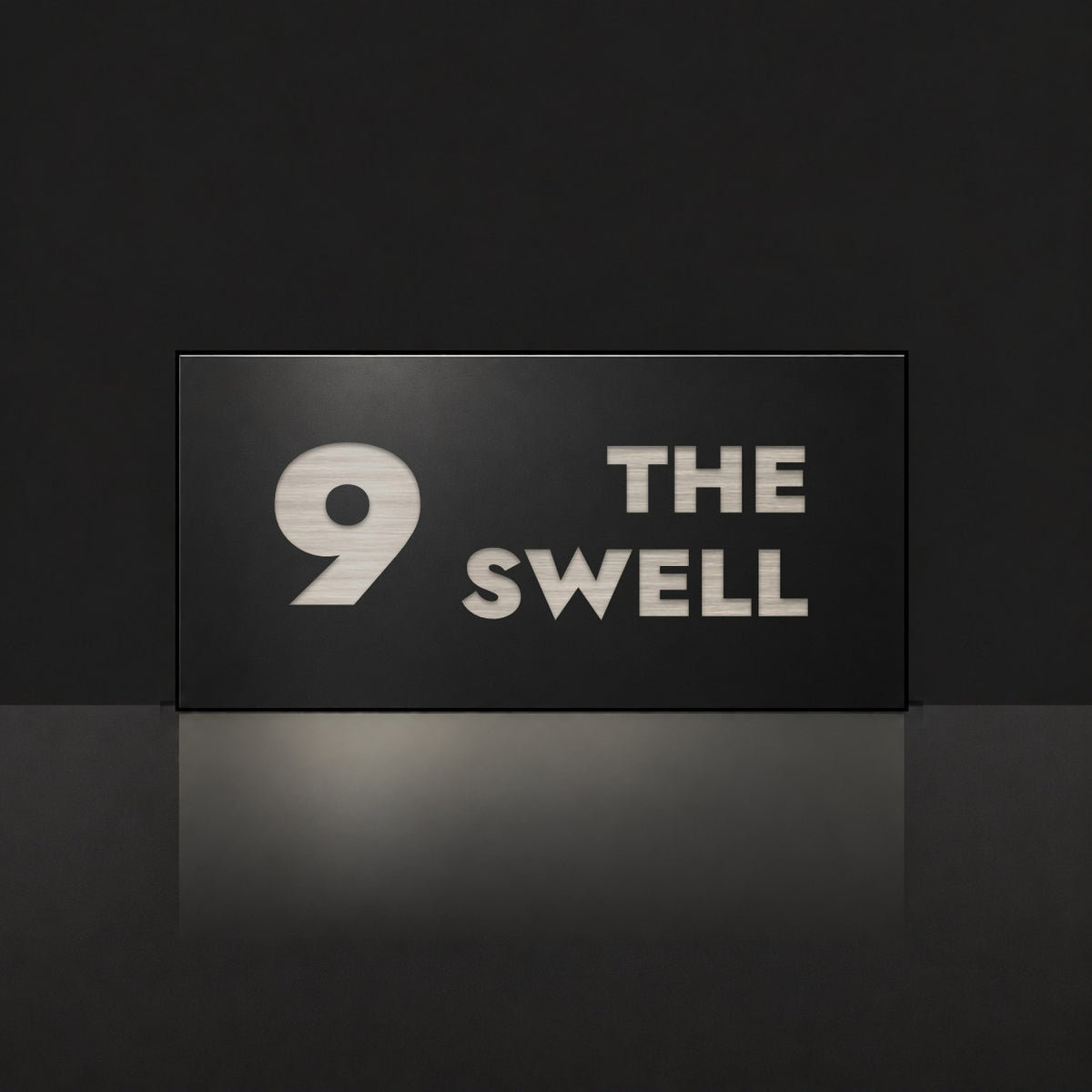 Brushed silver house number and street name sign with a brushed metal look, The Marcoola, black face reading 9 The Swell in silver lettering.