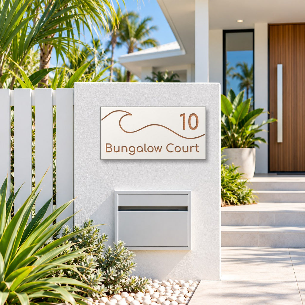 Brushed copper house number and street name sign with a brushed metal look, The Moffat, white face reading 10 Bungalow Court in copper lettering, with a wave, mounted on a white rendered fence above a white letterbox.