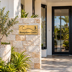 Brushed gold house number and street name sign with a brushed metal look, The Moffat, reading 3 Bungalow Court in black lettering, with a wave, mounted on a sandstone block pillar beside a glass front door.