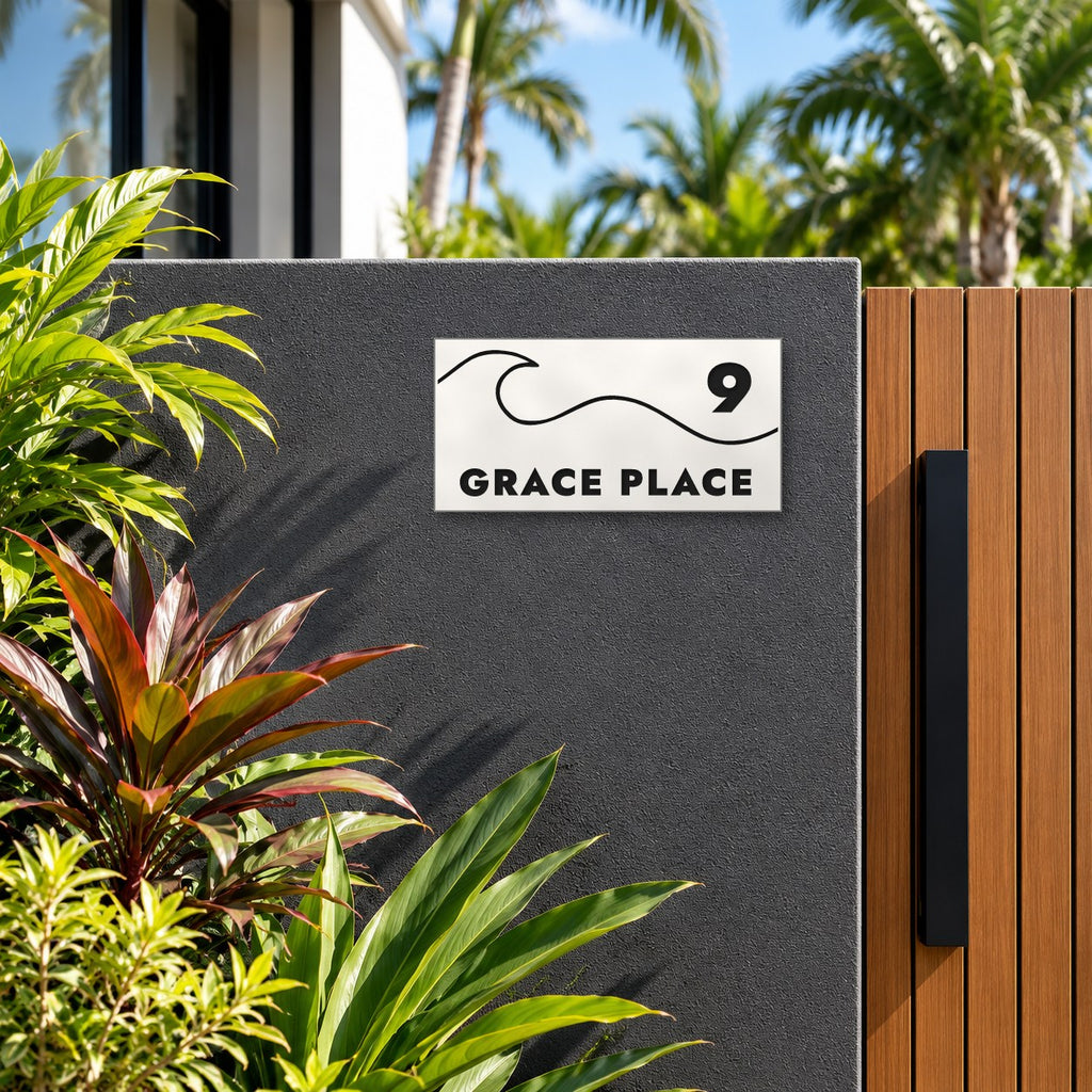 Matte white house number and street name sign, The Moffat, reading 9 Grace Place in black lettering, with a wave, mounted on a charcoal rendered wall beside a timber gate.