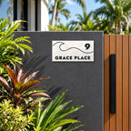 Matte white house number and street name sign, The Moffat, reading 9 Grace Place in black lettering, with a wave, mounted on a charcoal rendered wall beside a timber gate.