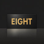 Brushed gold house number sign with a brushed metal look, The Montville, black face with the number spelled out as eight in gold lettering.