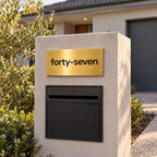 Brushed gold house number sign with a brushed metal look, The Montville, mounted on a rendered letterbox pillar above a black letterbox, the number spelled out as forty-seven in black lettering.
