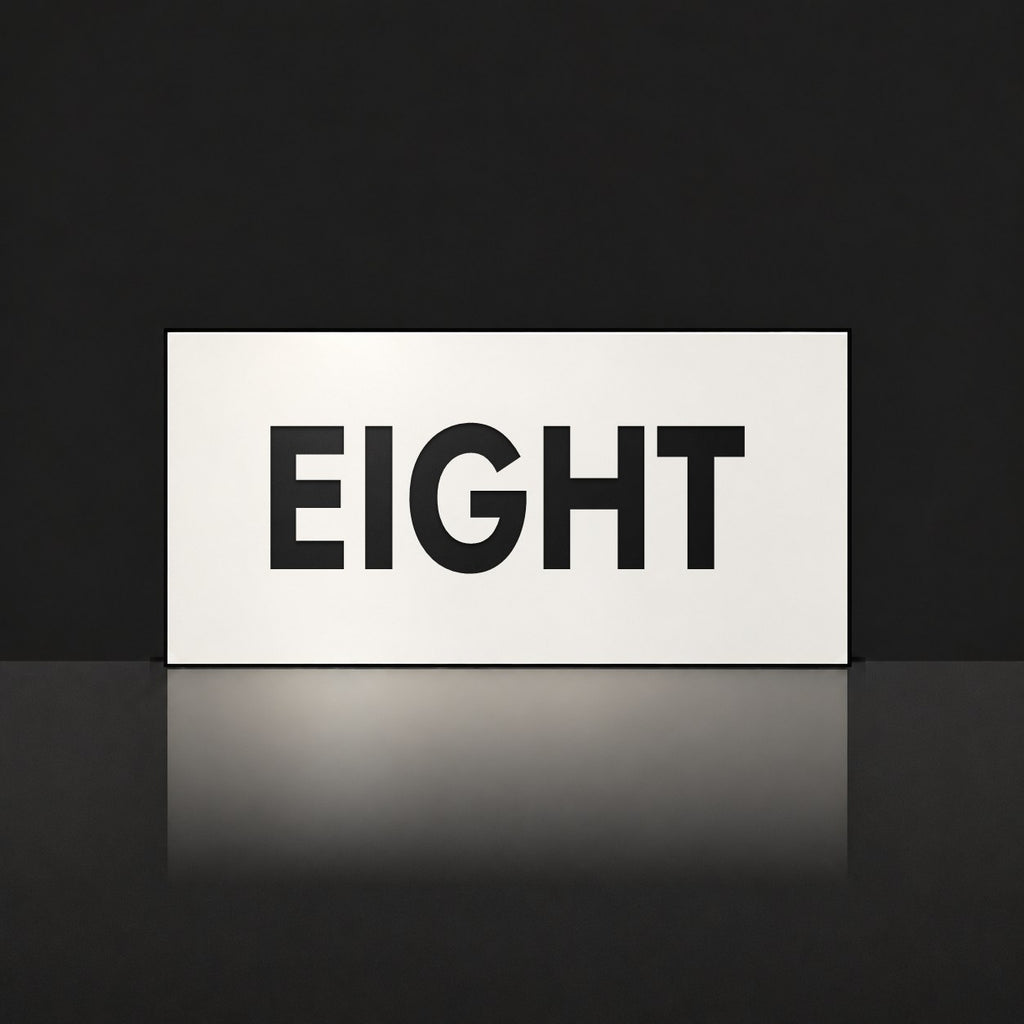 Matte white house number sign, The Montville, with the number spelled out as eight in black lettering.