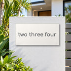 Matte white house number sign, The Montville, with the number spelled out as two three four in charcoal lettering, mounted on a white rendered front pillar.