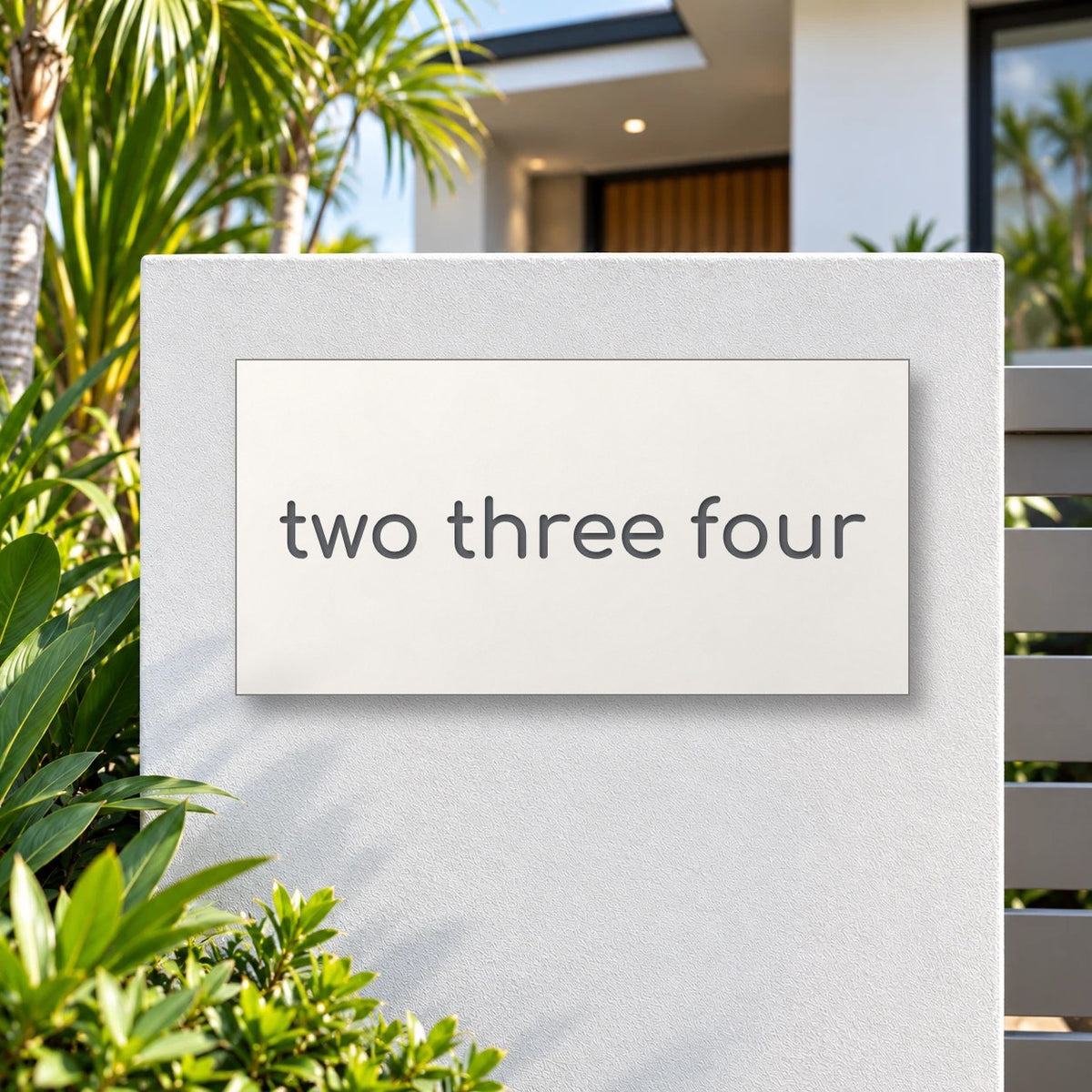 Matte white house number sign, The Montville, with the number spelled out as two three four in charcoal lettering, mounted on a white rendered front pillar.