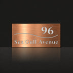 Brushed copper house number and street name sign with a brushed metal look, The Bokarina, reading 96 Sea Gull Avenue in white lettering, with a wave line.