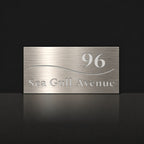 Brushed silver house number and street name sign with a brushed metal look, The Bokarina, reading 96 Sea Gull Avenue in white lettering, with a wave line.