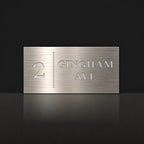 Brushed silver house number and street name sign with a brushed metal look, The Coolum, reading 2 Gingham Ave in white lettering, with a dividing line.