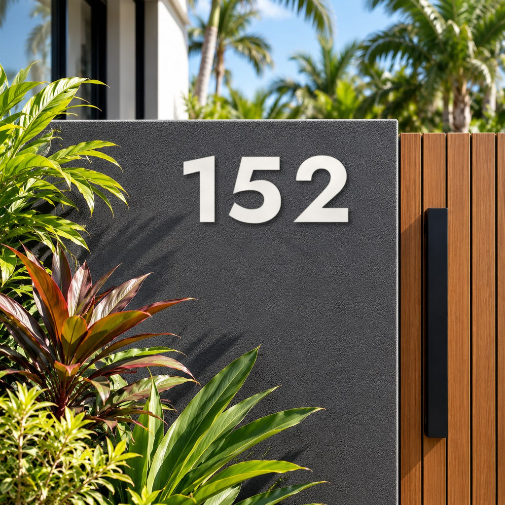 Matte white floating acrylic house number 152 in the bold font on invisible standoffs, on a charcoal rendered wall beside a timber gate.