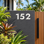 Matte white floating acrylic house number 152 in the bold font on invisible standoffs, on a charcoal rendered wall beside a timber gate.