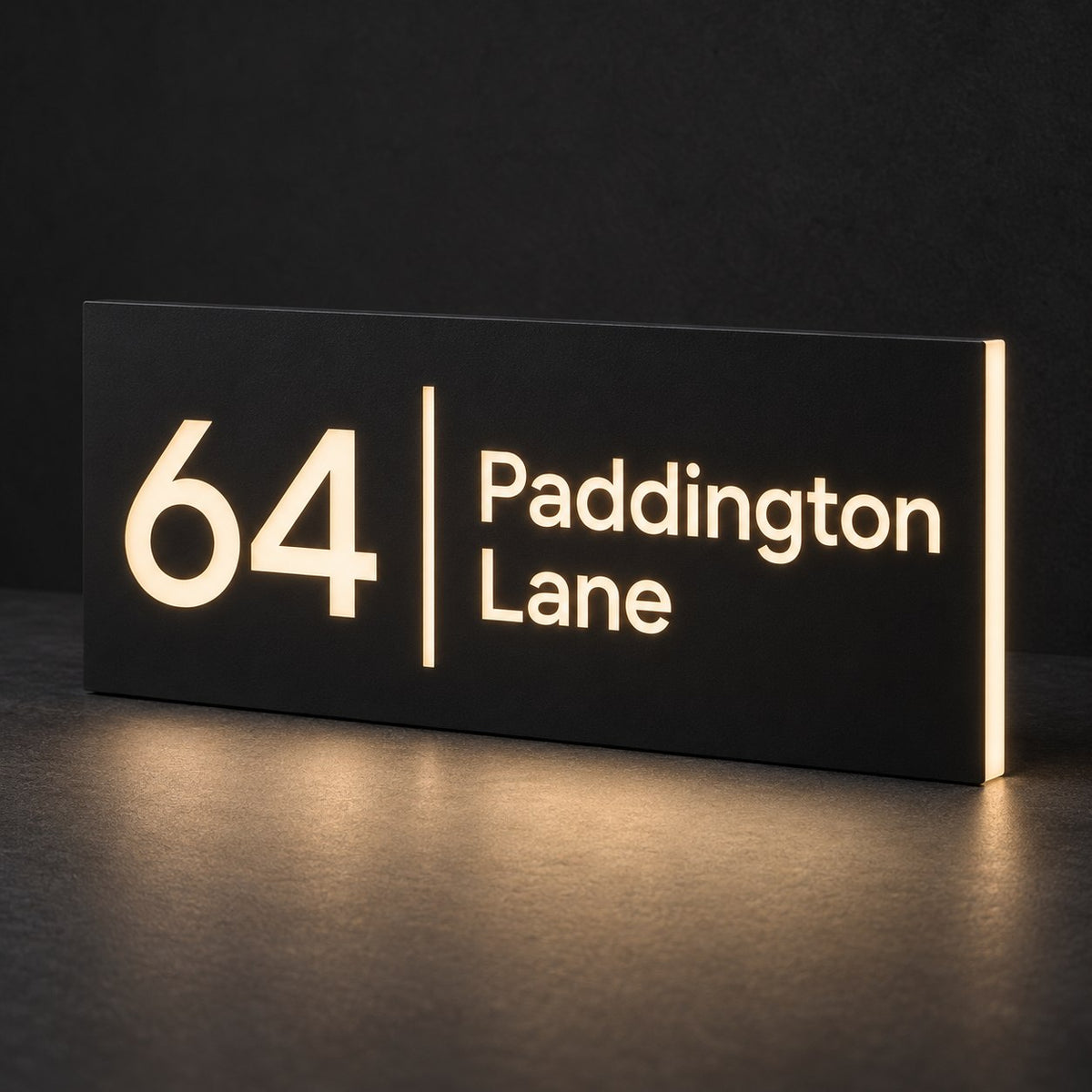 Matte black illuminated house number and street name sign, The Coolum, 64 Paddington Lane with the number, rule and street name cut through and lit from behind in warm white.